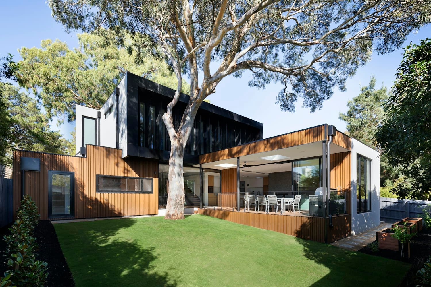 A modern home with a designed backyard — lawn, mature tree, planting beds and an outdoor dining area