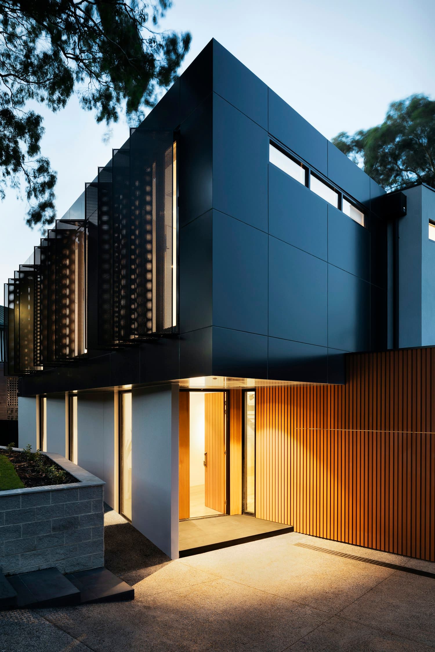 A paved home entry at dusk with a raised planter and warm landscape lighting