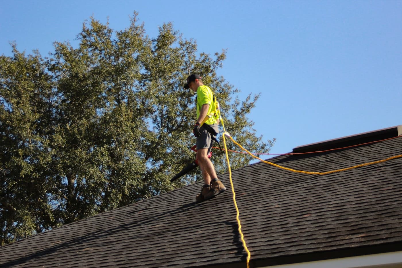 A roofer walking on a residential asphalt-shingle roof under a clear blue sky