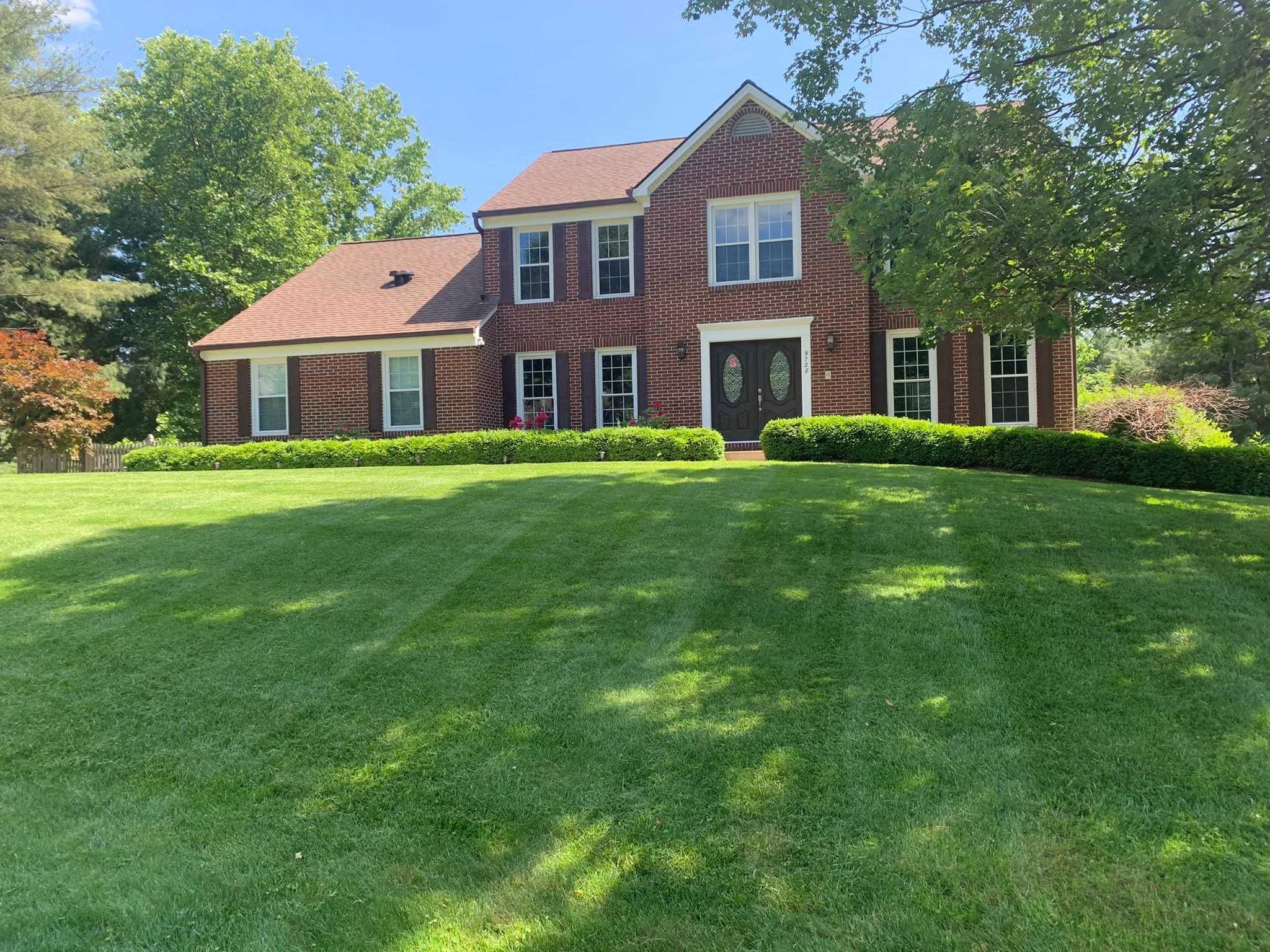 Wide manicured front lawn in front of a red brick colonial house
