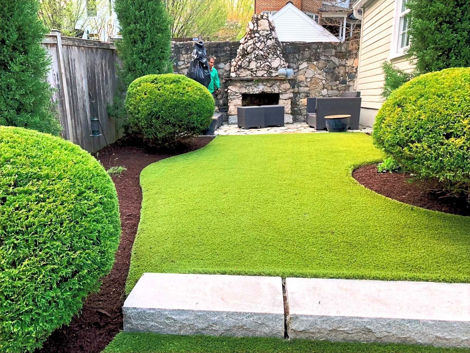 Clipped boxwood, shaped lawn and a stone fireplace in an enclosed rear garden