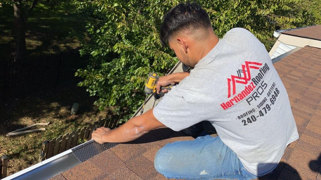 Oakline Roofing Pros crew member in a branded t-shirt installing gutter guard on a residential roof